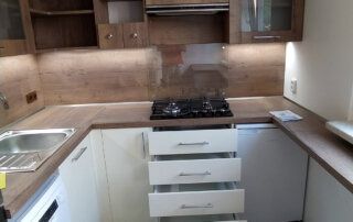 Moderní kuchyň rekonstruovaná na míru s dřevěnými prvky, plynovou varnou deskou, bílými skříňkami a praktickým úložným prostorem, navržená společností RAST Kutná Hora.