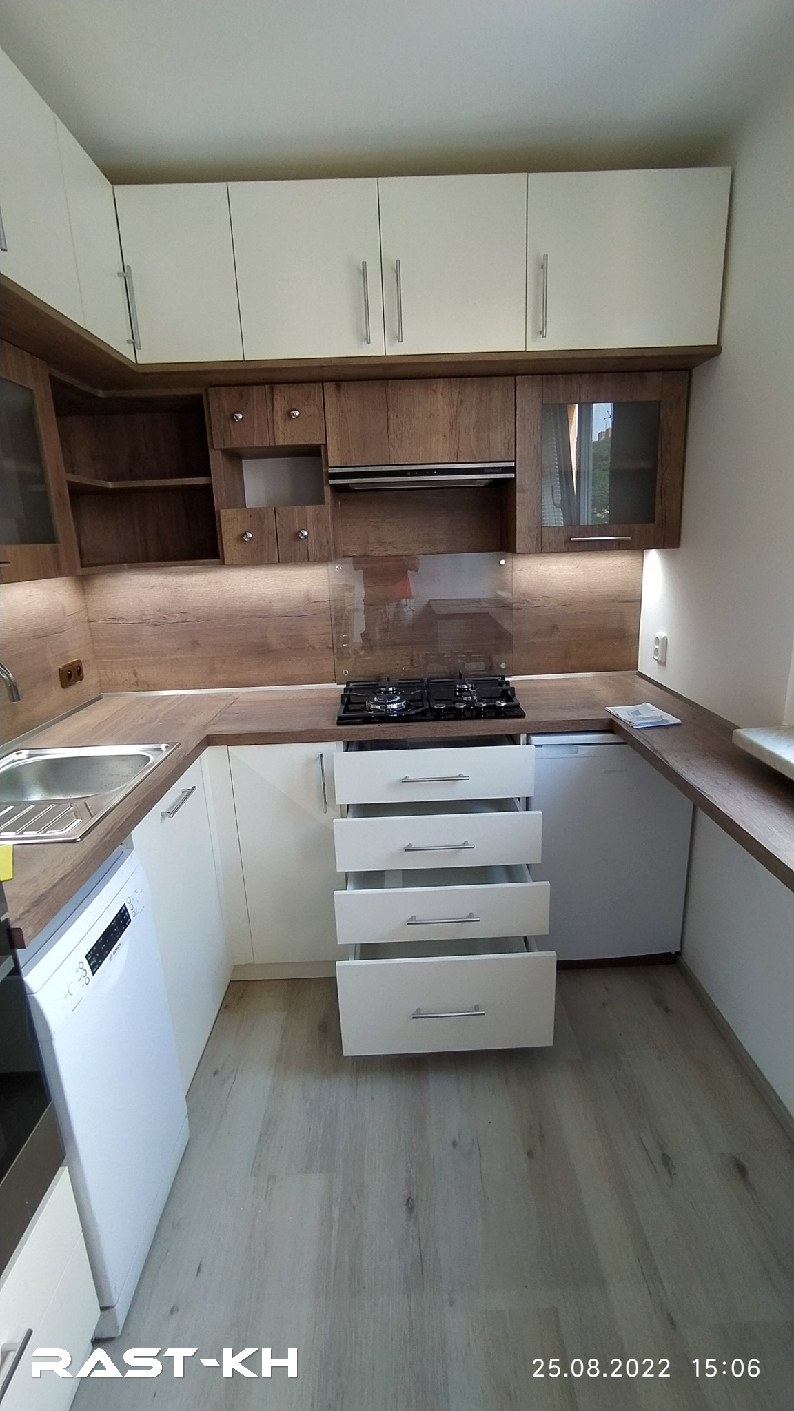 Moderní kuchyň rekonstruovaná na míru s dřevěnými prvky, plynovou varnou deskou, bílými skříňkami a praktickým úložným prostorem, navržená společností RAST Kutná Hora.